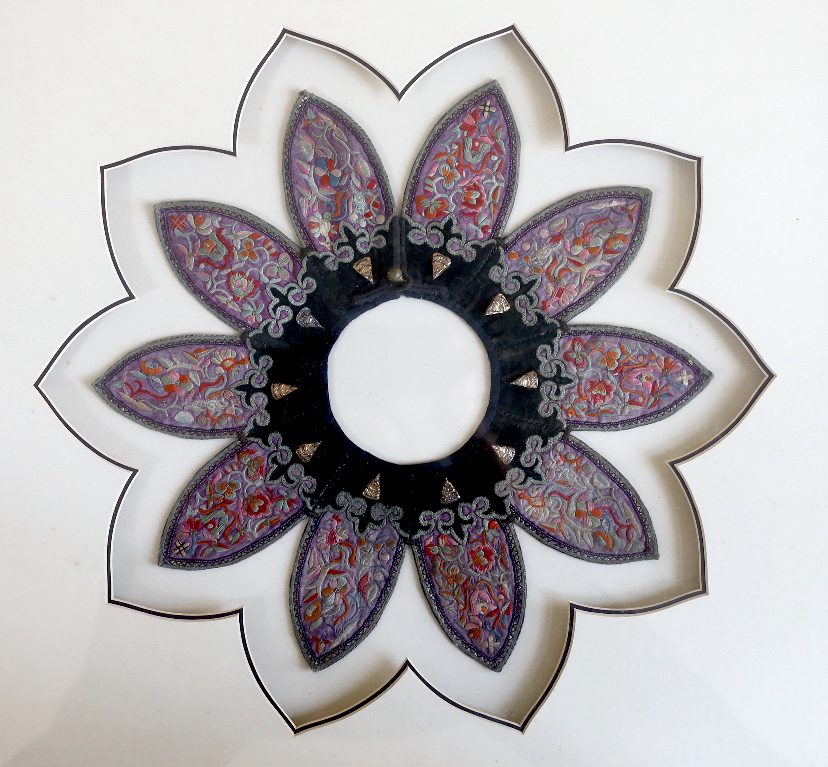 A late 19th century Chinese black velvet and purple silk embroidered collar, petal shaped, with metal appliqué edges and ten gold coloured metal ornamental attachments, 34cm round